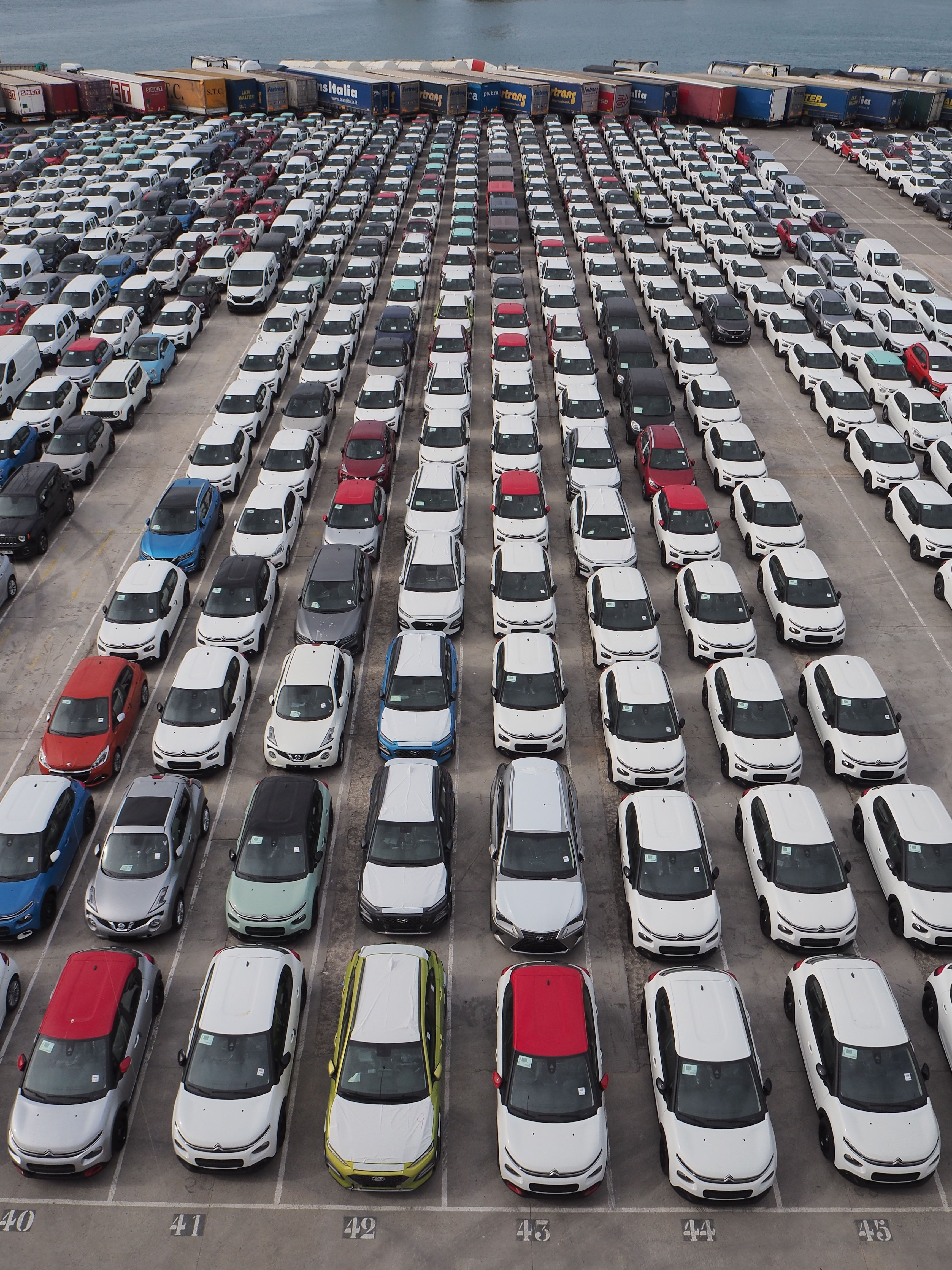Top-down view of new cars parked in numbered rows at a vehicle port terminal
