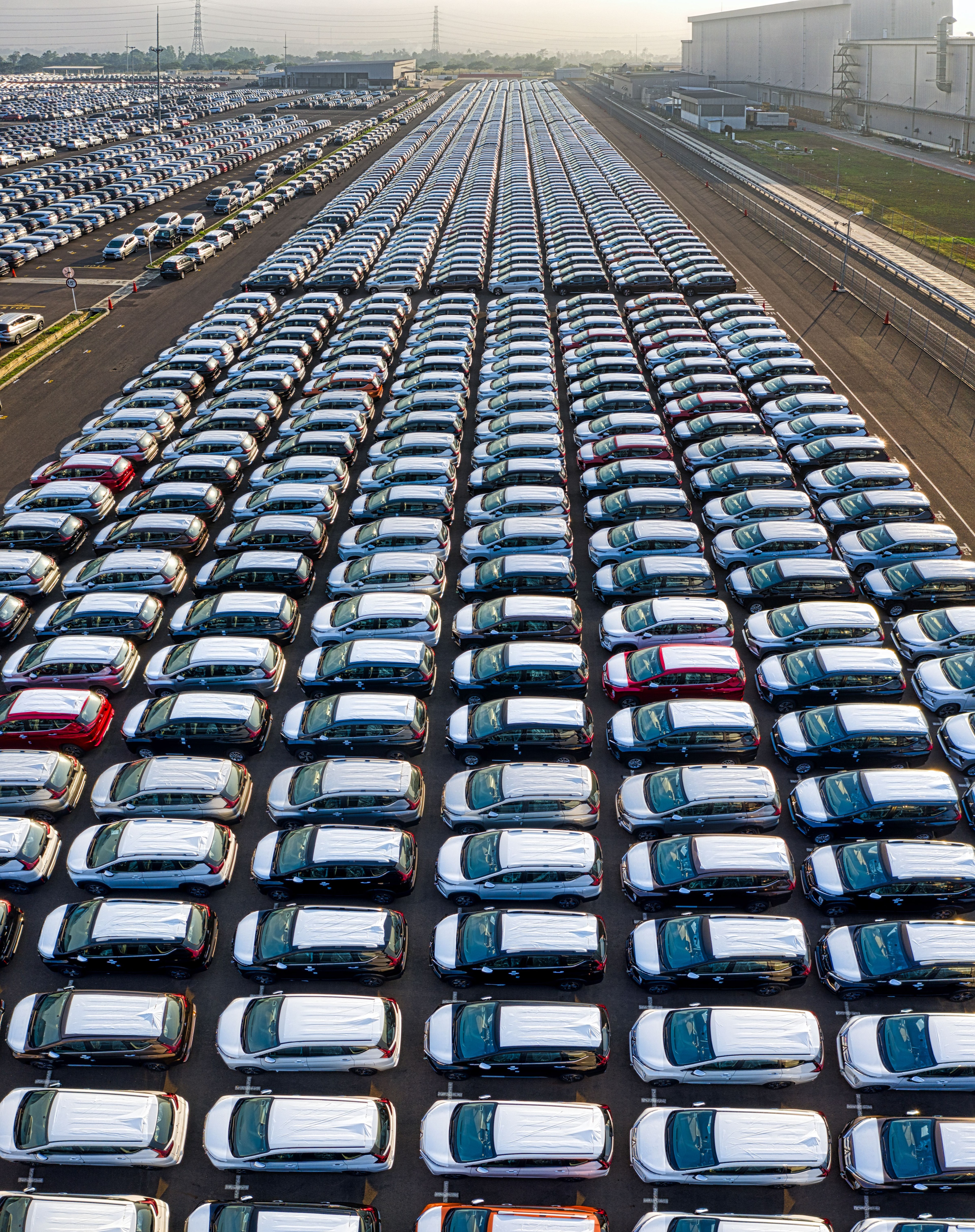 Rows of new cars stretching toward the horizon at a vehicle distribution yard at sunrise